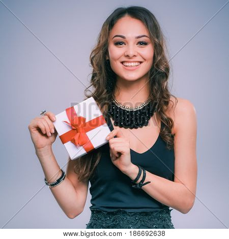Young woman holding a gift box isolated on gtay background