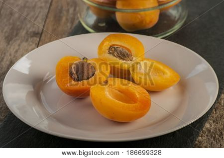 Whole orange apricots with red blush, from above, space for text. Open apricot with stone and leaves. On rustic white wood.