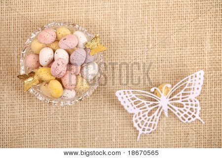 easter chocolate speckled eggs in bowl with paper batterfly on hessian table, shallow dof
