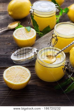 Fresh homemade lemon curd in glass jars on rustic wooden background. Selective focus.