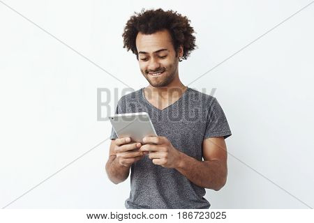 Interested handsome african man looking at tablet over white bakground. Copy space.