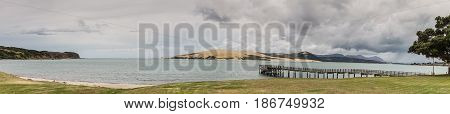 Bay of Islands New Zealand - March 7 2017: Panorama shot of exit to Tasman Sea from Hokianga Harbour shows large dune pier mountains all under heavy cloudscape because of approaching cyclone.