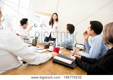 Asian business woman presenting work to mixed race colleagues in the meeting
