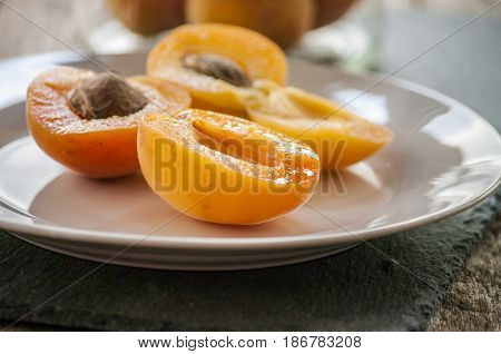 Whole orange apricots with red blush, from above, space for text. Open apricot with stone and leaves. On rustic white wood.