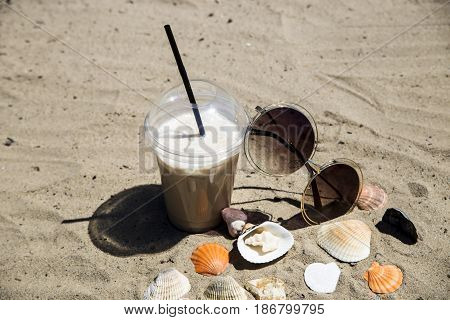 Ice latte on sand with cockleshells and glasses