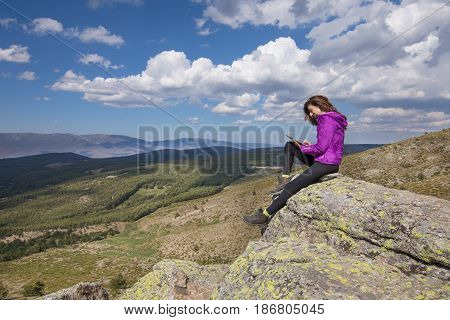 Woman On Top Of Mountain Typing In Tablet