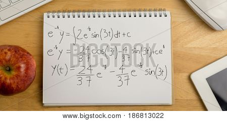 Calculations against black background against overhead of notepad and technology