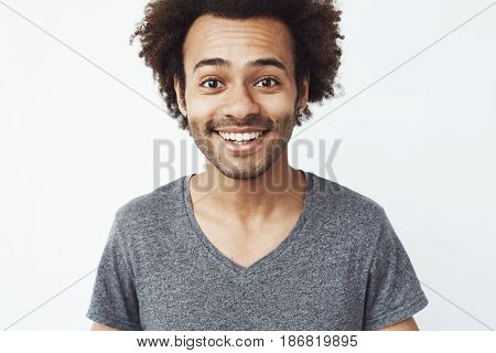Close up portrait of happy and charming african guy smiling at camera, a boyfriend waiting for a date, or a head hunter dream standing over white wall. Copy space.