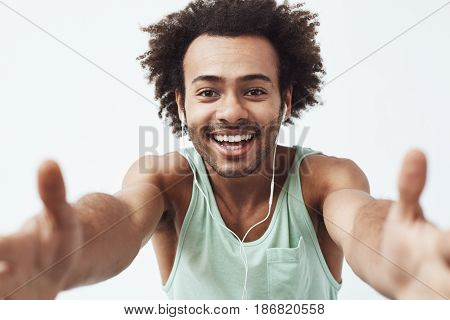 Cheerful young african man in headphones smiling stretching hands to camera. White background.