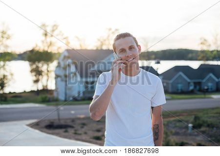 Caucassian young man in a white tshirt works from home talks on the phone to close an important start up deal on a sunny evening in usa