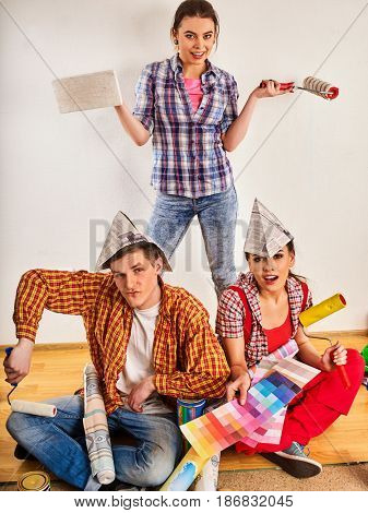 Repair group of people building home using paint roller tools. Woman and man in newspaper cap holding color guide renovation apartment.