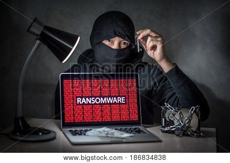 Hacker holding the key with laptop computer screen showing ransomware attacking alert in red digital binary background with hard disk drive lock. Cyber attack concept