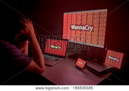 Young Asian male frustrated confused and headache by WannaCry ransomware attack on desktop screen notebook and smartphone cyber attack internet security concept