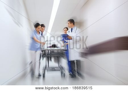 health care, reanimation and medicine concept - group of medics or doctors carrying unconscious woman patient on hospital gurney to emergency (motion blur effect)