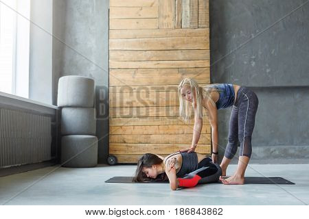 Yoga class teacher and beginner making asana exercises. Instructor assists to make cobbler pose, baddha konasana. Healthy lifestyle in fitness club. Stretching with coach