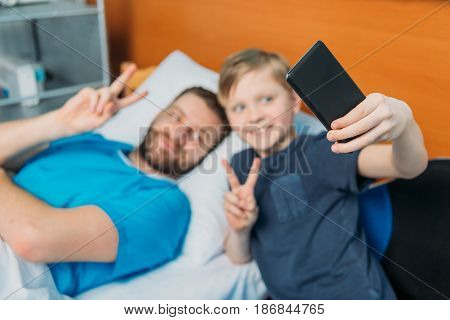Young Father And Son Taking Selfie On Smartphone At Ward, Hospital Patient Care