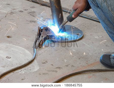 Soft focused picture of Worker man is welding round steel pipe and footplate by welding machine in factory