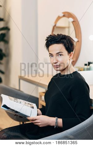 Attractive woman primp at the mirror with lamps in the beauty studio. A happy satisfied customer of make-up and hairstyle service.