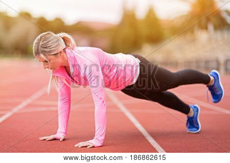 side view of young slim attractive woman doing plank exercise at outdoor stadium core training and fitness concept sun flare