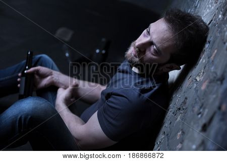 Apathy of my soul. Depressed reckless hopeless man sitting on the floor in the basement while expressing sadness and drinking alcohol