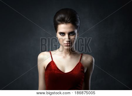 Beautiful woman with evening make-up and updo. Fashion photo. Girl wearing red dress ower dark background. Studio shoot.