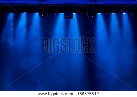 The blue light from the spotlights through the smoke in the theatre during the performance. Lighting equipment.