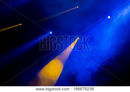 The blue-orange light from the spotlights through the smoke in the theatre during the performance. Lighting equipment.