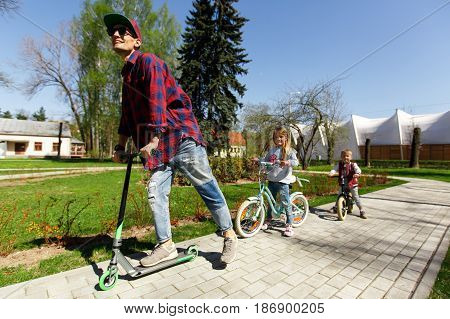 Young father with children on scooters in park during day