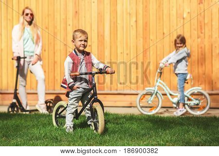 Woman with children on bicycles against wooden wall in afternoon in spring