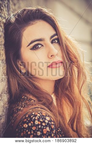 Beautiful woman close portrait. A charming and attractive young woman looking with intense sensuality and femininity. Leaning on a wall.