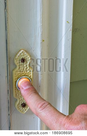 Male finger preparing to ring a doorbell to a front door with a white frame on a green house