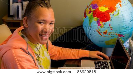 Teenager studying at the table with laptop and a globe