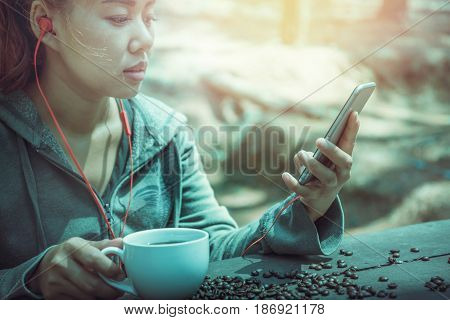 Women drink coffee Play mobile phone On the wooden table floor there is a coffee bean.