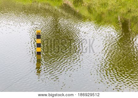 Water level pole indicating water depth of natural lake in summer.