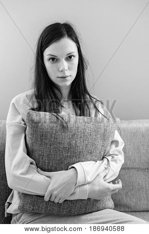 Lonely depressed woman at home, she is sitting on the sofa and hugging a pillow