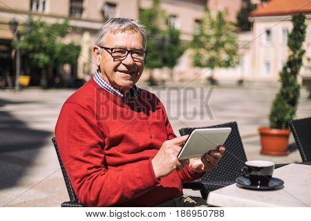 Senior man using digital tablet while drinking coffee at the bar.