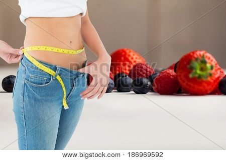 Digital composite of Midsection of woman measuring waist by fruits representing weight loss