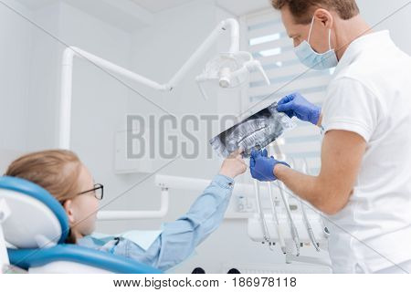 Get the idea. Distinguished charming skillful dentist showing his patient an xray of her teeth and making sure she understating everything