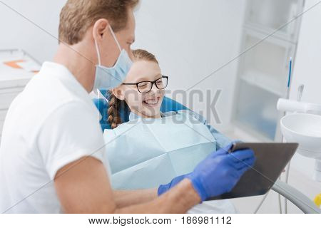 Charismatic teacher. Handsome friendly inventive doctor giving the girl a lecture on dental hygiene and using his garget as helping tool while the child seeming fascinated