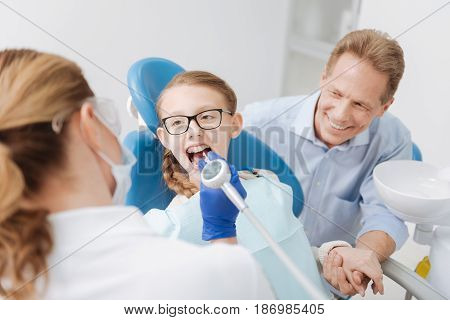 Great parent. Precise wonderful clever dentist conducting a procedure employing professional equipment while the parent sitting beside his girls and supporting her