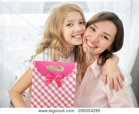 Pretty Girl Hugging Her Beautiful, Young Mother. Child Giving Present To Her Mom For Holiday. Happy 