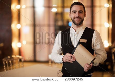 Waist Up Portrait Of Handsome Waiter Smiling Cheerfully At Camera Standing In Luxury Restaurant Or C
