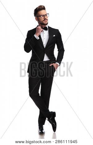 Elegant man arranging his bow-tie while standing with his legs crossed