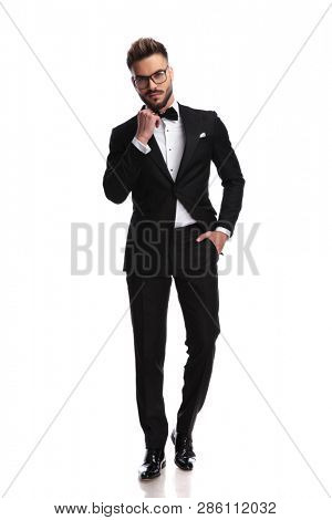 Ellegant man arranges his bow-tie with a hand in his pocket while standing