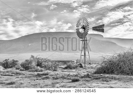 An Early Morning Landscape, With A Windmill And Dam, In The Tankwa Karoo Of South Africa. Monochrome