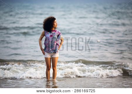 Young asian woman stands on the surf line of sea.