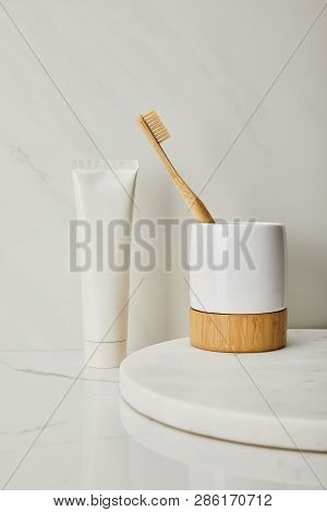 Holder With Bamboo Toothbrush And Toothpaste In Tube On White Marble Background