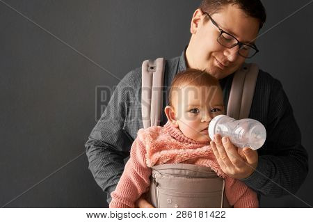 Fathre And His Kid In Baby Carrier At The Grey Background Wall, Baby Wearing Concept