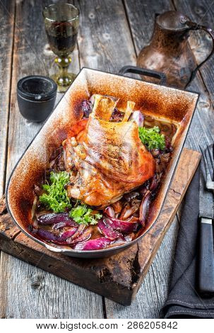 Traditional Bavarian schweinshaxe with onion as closeup in a rustic stewpot on an old wooden board 