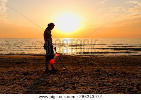 Man Silhouette With Metal Detector On Sunset On The Beach